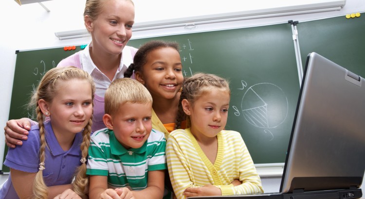 Portrait of pupils looking at the laptop with teacher near by